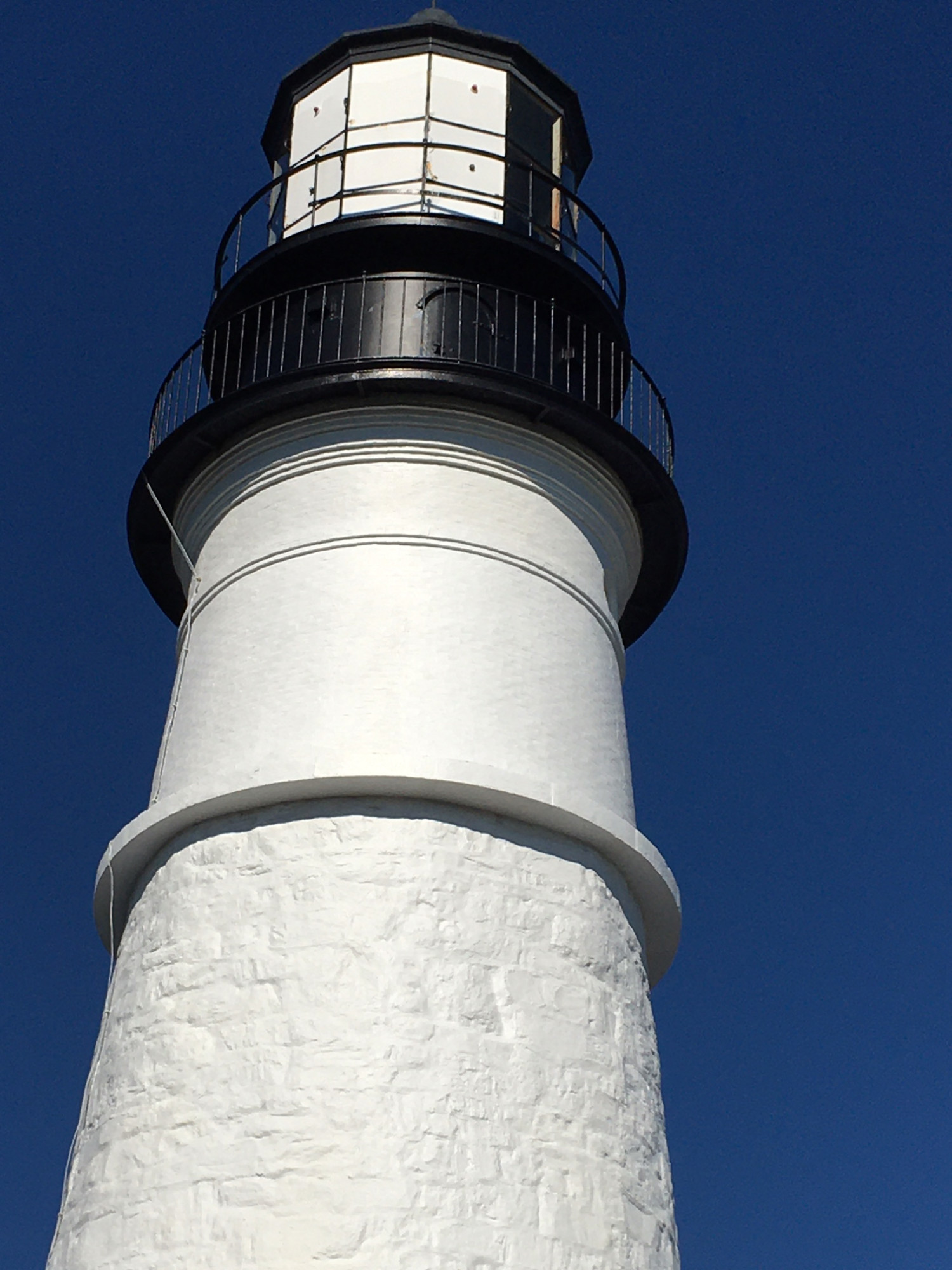 Looking up at a white lighthouse tower with the blue sky.