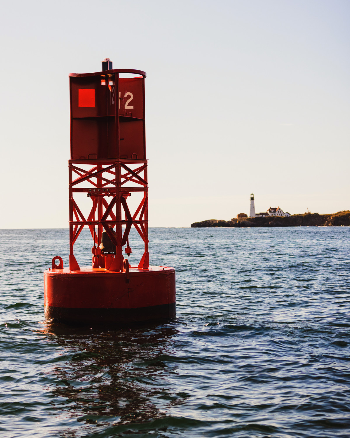Red navigational bell buoy with Portland Head Lighthouse in the background